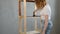 The woman paints wooden book shelf With Brush In brown Color.