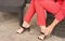 A woman in a pantsuit the color of live coral sits in a chair and straightens the clasp on sandals.