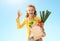 Woman with paper bag with groceries showing ok against blue sky