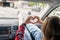 Woman passenger, legs in a jeans and socks on car dashboard while travel on the highway.  Girl showing sign heart hand. Freedom
