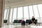 Woman passenger wearing black clothes, sitting on chair seat in transit lounge of airport terminal, stretching legs.