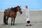 Woman patting horse on beach by the sea.