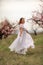 Woman peach blossom. Happy woman in white dress walking in the garden of blossoming peach trees in spring