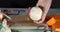 Woman peels onions on a wooden board in the kitchen. Female hands prepare cream soup with pumpkin and and onions