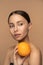 Woman with perfect face skin, combed hair, holding orange. Portrait of female with natural makeup and citrus fruit posing over