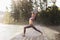 A woman performs the virabhadrasana exercise, the first warrior pose, practices yoga, stands in the morning on a wooden bridge