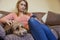 Woman With Pet Cockapoo Dog Relaxing On Sofa Checking Mobile Phone At Home
