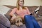 Woman With Pet Cockapoo Dog Relaxing On Sofa Watching TV At Home