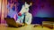 A woman in a pigeon mask is dancing in the background, and a young man in a unicorn mask is sitting at a table