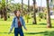 A woman with pigtails in jeans and a plaid shirt stands among tall palm trees on a lawn in a spacious park. Spring walk.