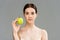 Woman with pimples on face holding green apple  on grey