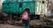 A woman with a pink backpack is standing in the background of a green wagon with wheels