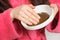 A woman in a pink bathrobe holds a plate with a hair or face mask, an Ayurvedic blend of herbs for skin care at home.