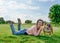 Woman in pink coat, black top and jeans listens to music / audiobook and rest with dogs on meadow on sunny spring warm day