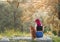 A woman with pink hair enjoys with a Shiba Inu dog on a stone in a lush grove.