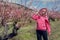 woman in a pink hoodie and a hair wig stands on a peach field with flowers in spring