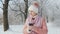 A woman in a pink jacket enjoys a walk in a winter park. Uses a mobile phone