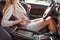 Woman in pink jacket fastens her seat belt in summer in passenger compartment. Automatic gearbox, steering wheel and