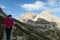 A woman in pink jacket hiking on a narrow path in Italian Dolomites. There are sharp and steep mountains around her.