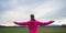 Woman in pink jacket standing with her arms wide open under an evening sky