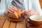 Woman with pink manicure is tearing a small piece from large croissant, front