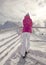 Woman in pink ski jacket leaning on snow covered rail, looking a