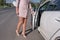 A woman in a pink suit opens the car door, in the summer in the city, business taxi, tanned skin, long legs, high-heeled