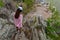 Woman in pink sweater standing by edge of cliff with climbers ropes