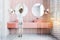 Woman in pink tile bathroom with double sink