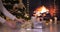 Woman placing gifts under Christmas tree near fireplace