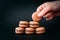 Woman placing macaroons on heap on black background