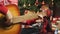 Woman is playing Christmas song on acoustic guitar sitting on floor near decorated New Year tree in garland lights. Happy family c