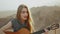 Woman playing guitar and singing in desert in sunset landscapes, desert mountains background, 4k