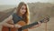 Woman playing guitar and singing in desert in sunset landscapes, desert mountains background, full hd