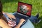 Woman playing poker on laptop pc computer, sitting in park on green grass sunshine lawn outdoors.