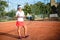 Woman playing tennis on clay court with tennis racket, balls and white outfit