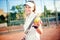 Woman playing tennis, holding racket and ball. Attractive brunette girl wearing white t-shirt and cap on tennis court