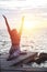 Woman playing yoga pose on beach pier against sun rising sky