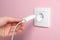 Woman plugging charger into power socket on pink wall, closeup. Electrical supply