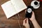 Woman plugging earphones into phone over wooden table with book, top view