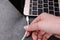 Woman plugging USB cable with lightning connector into laptop port on dark table, closeup