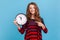 Woman pointing big clock and looking at camera with positive, showing wall watches to hurry up.