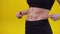 Woman points fingers at a muscular belly in the studio, close-up. Sporty woman shows off muscular stomach, yellow