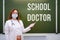 Woman points to the blackboard with the text School Doctor. Concept of problems at school during the coronavirus epidemic