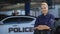 Woman police officer smiling, standing near patrol car with crossed hands, law