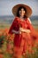 Woman poppy field red dress hat. Happy woman in a long red dress in a beautiful large poppy field. Blond stands with her