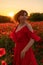 Woman poppy field red dress sunset. Happy woman in a long red dress in a beautiful large poppy field. Blond stands with