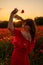 Woman poppy field red dress sunset. Happy woman in a long red dress in a beautiful large poppy field. Blond stands with