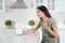 Woman with portable fan suffering from heat in kitchen. Summer season