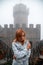 Woman portrait. feels the cold. Fortification on top of the mountain, old castle on background. Journey. Mystical atmosphere, fog